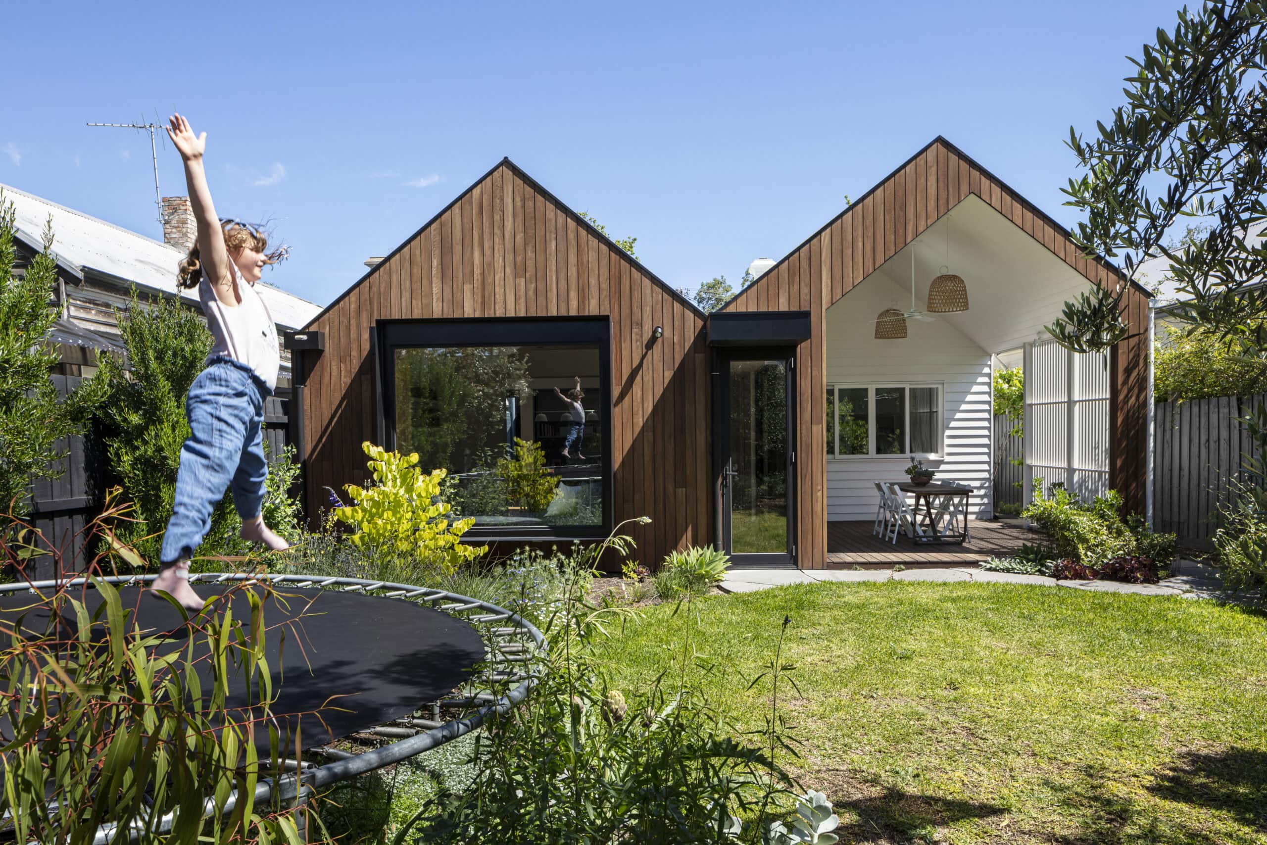 Child on a garden trampoline in front of the twin-gabled timber extension and outdoor dining area.