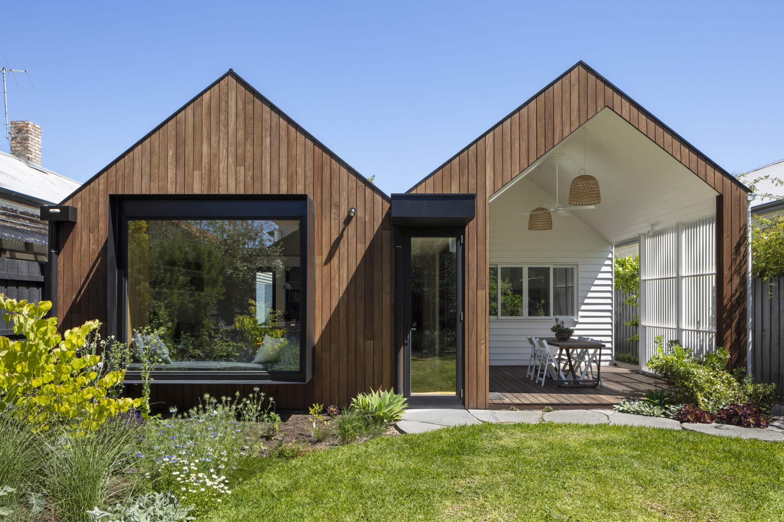 Twin timber-clad gables framing a large living-room window and a sheltered outdoor dining area.
