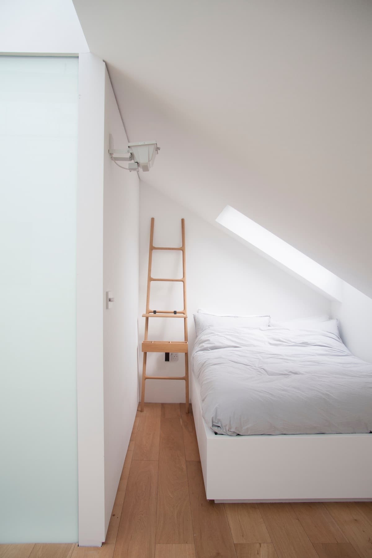 White walls and timber flooring define a bedroom beneath the sloping roof at Vertical Intersect.