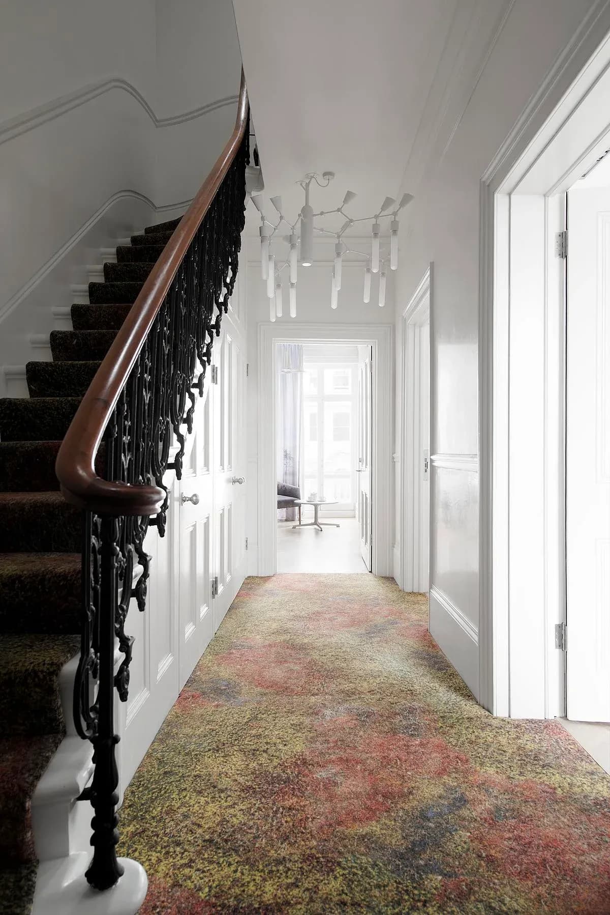 Landscape imagery continues along the stair carpet beside the iron balustrade.