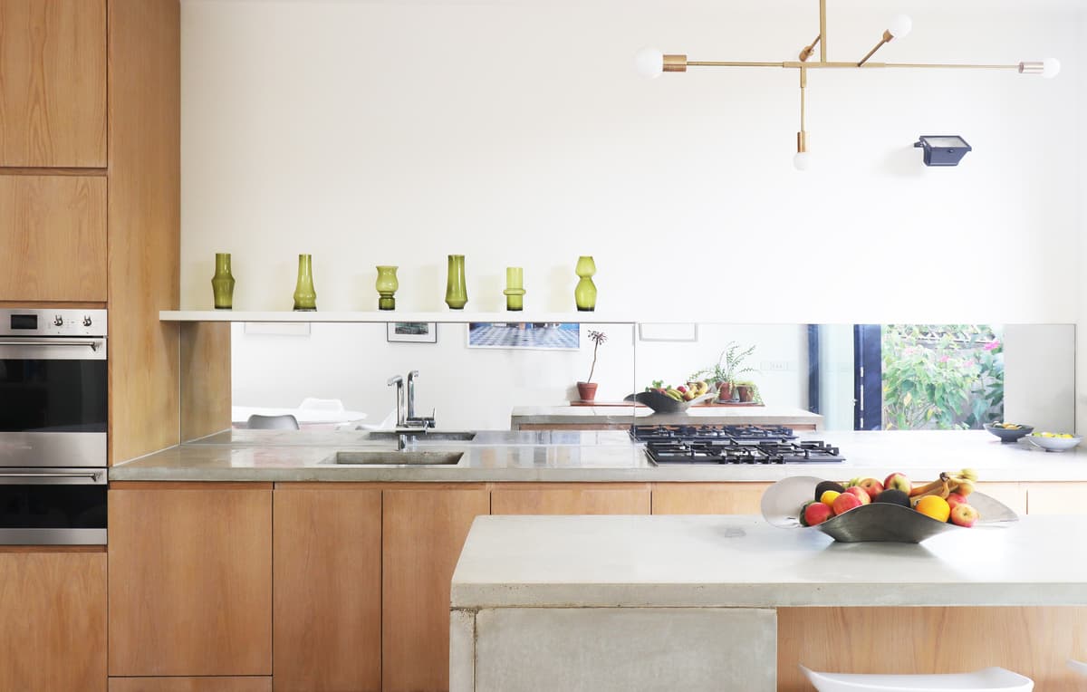 Timber cabinetry, a mirrored splashback and a pale island define the kitchen at Structuralist House.