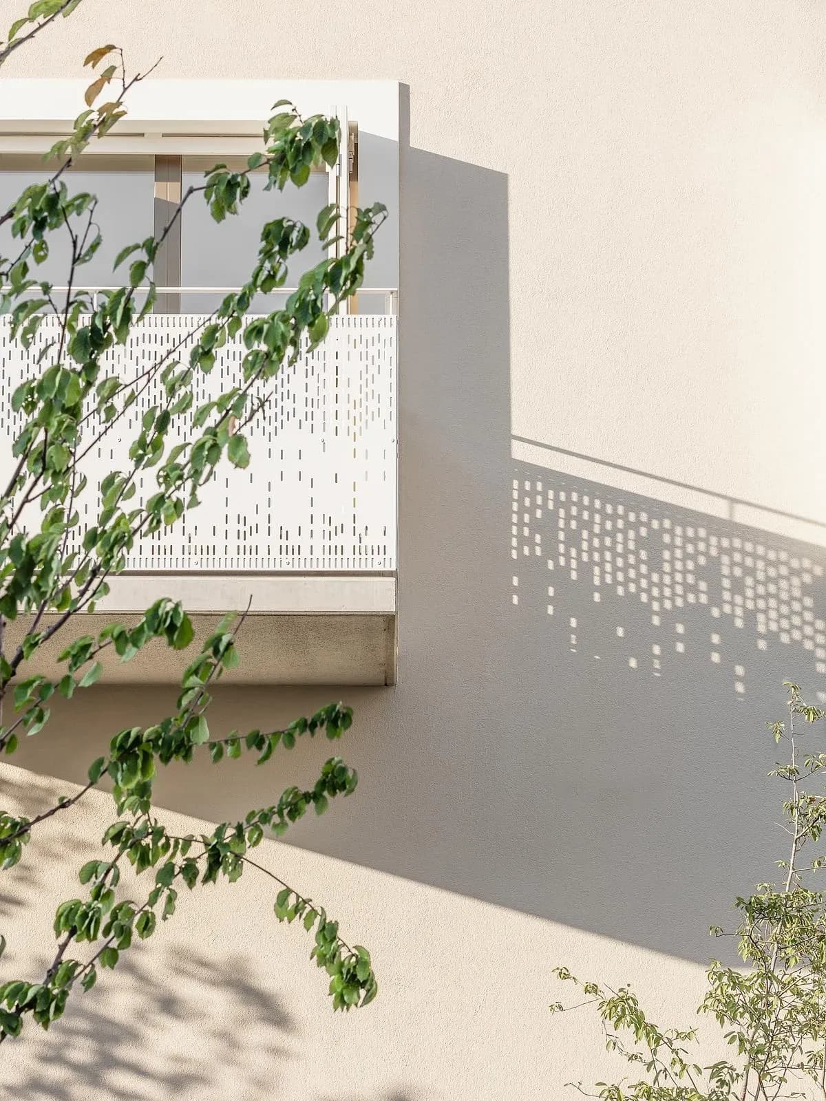 A perforated balcony balustrade casts a dotted shadow across the facade.