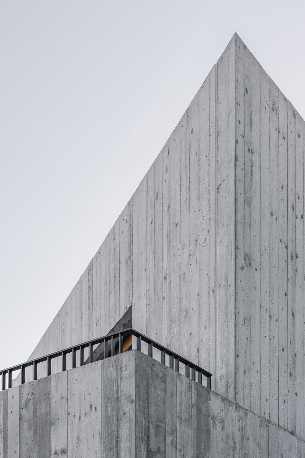 Board-formed concrete and narrow openings articulate the taller end of the building.
