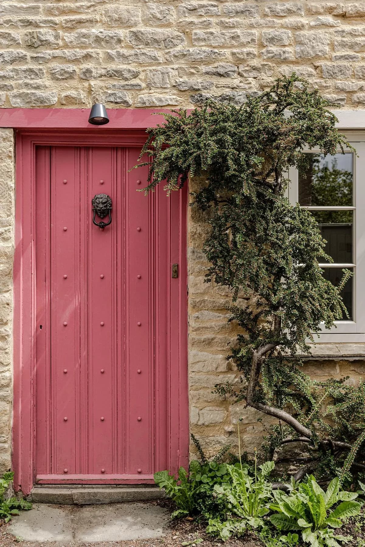 A pink-painted front door with a lion's-head knocker, set into the cottage's stone wall.