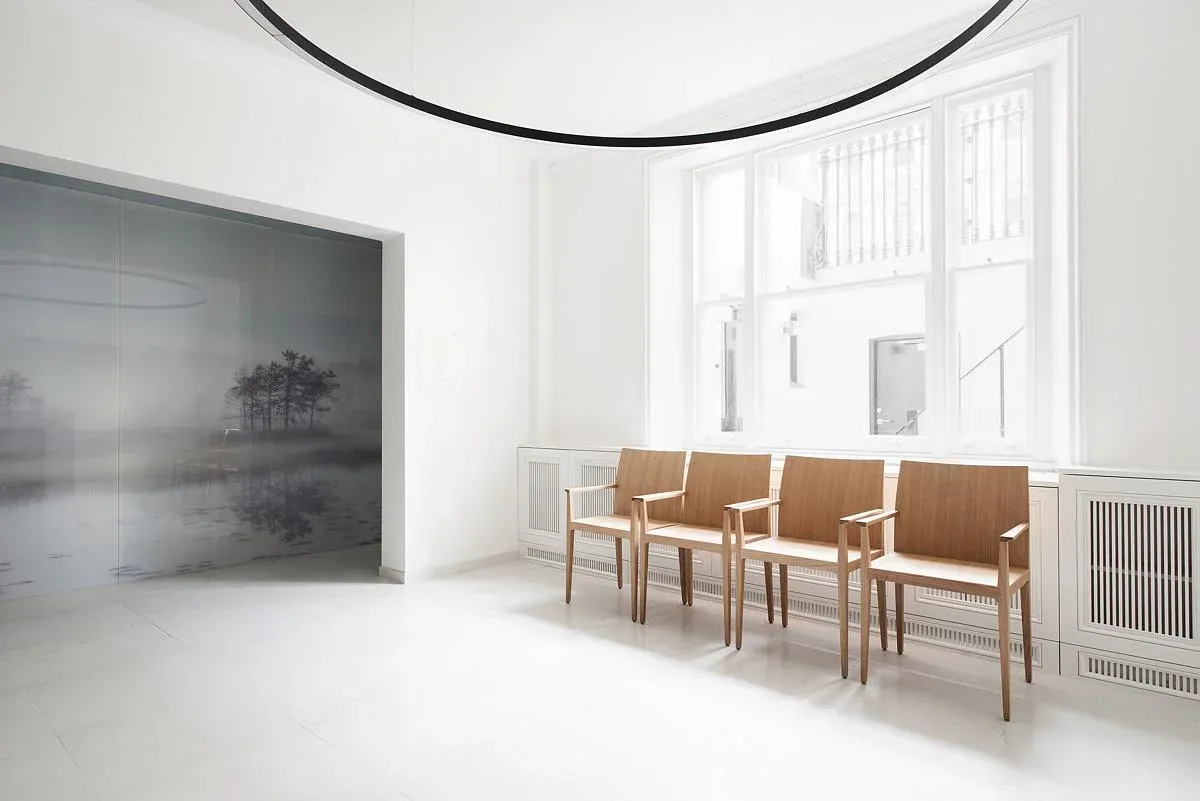 A circular pendant hangs above timber chairs beside a landscape wall image.