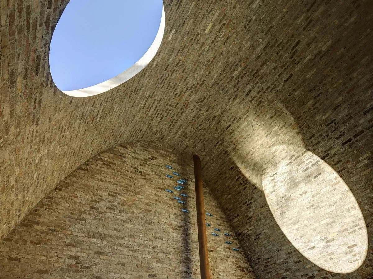 Sunlight draws the skylight’s elliptical outline across the brickwork.