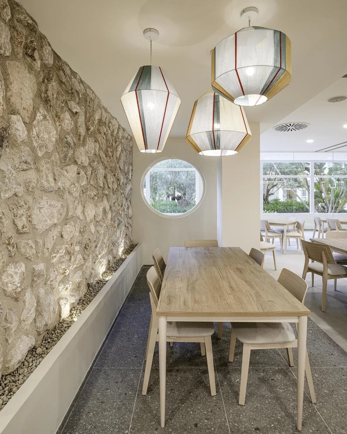 Woven pendant lights hang over a long table beside a rough stone wall.