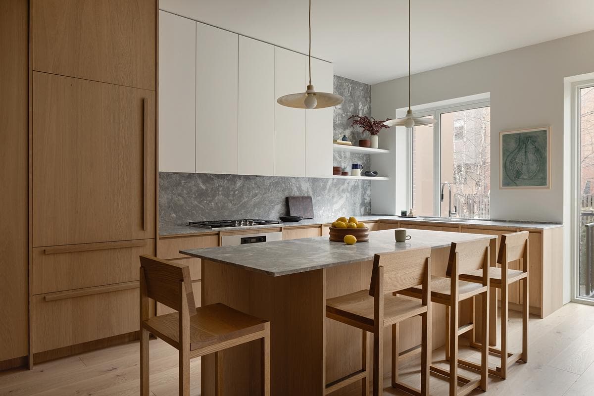 Custom oak cabinetry frames a kitchen island and pale stone surfaces.