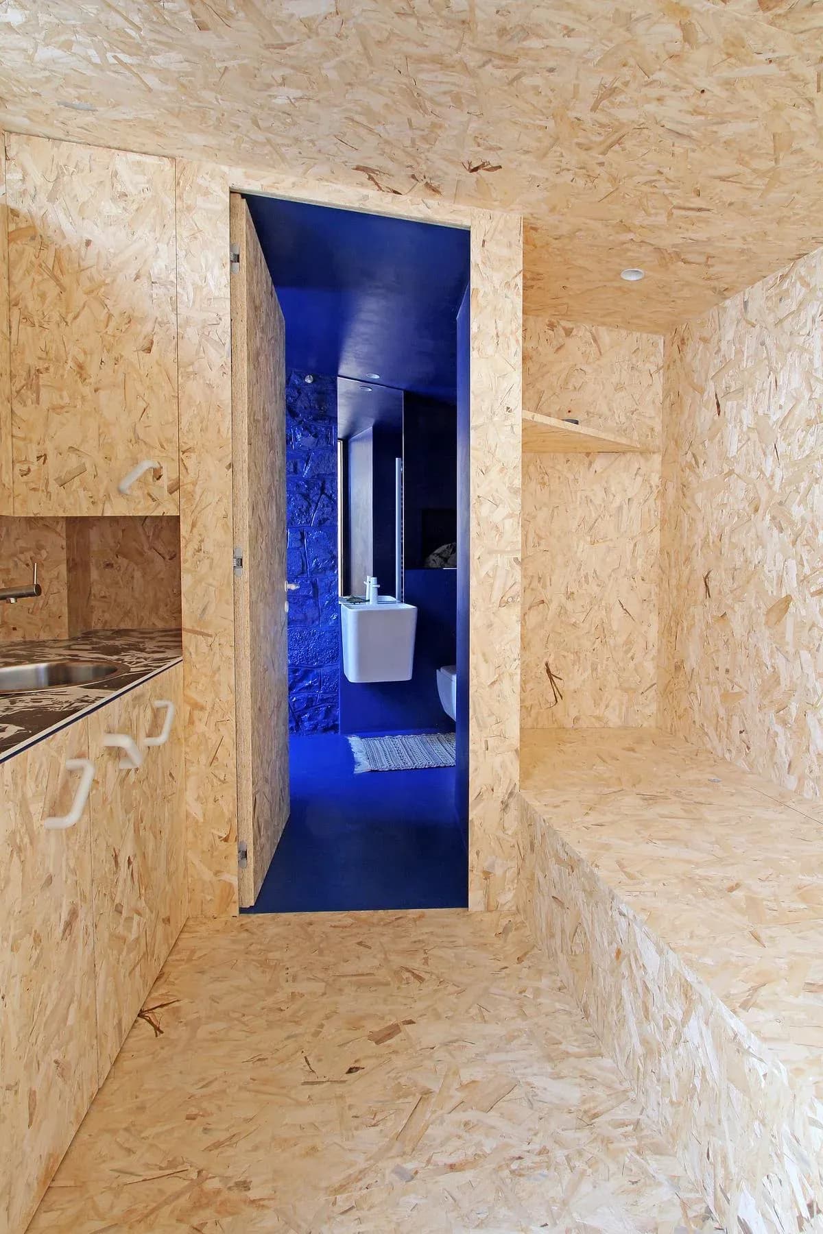Timber-lined openings lead from the living area towards the blue bathroom.