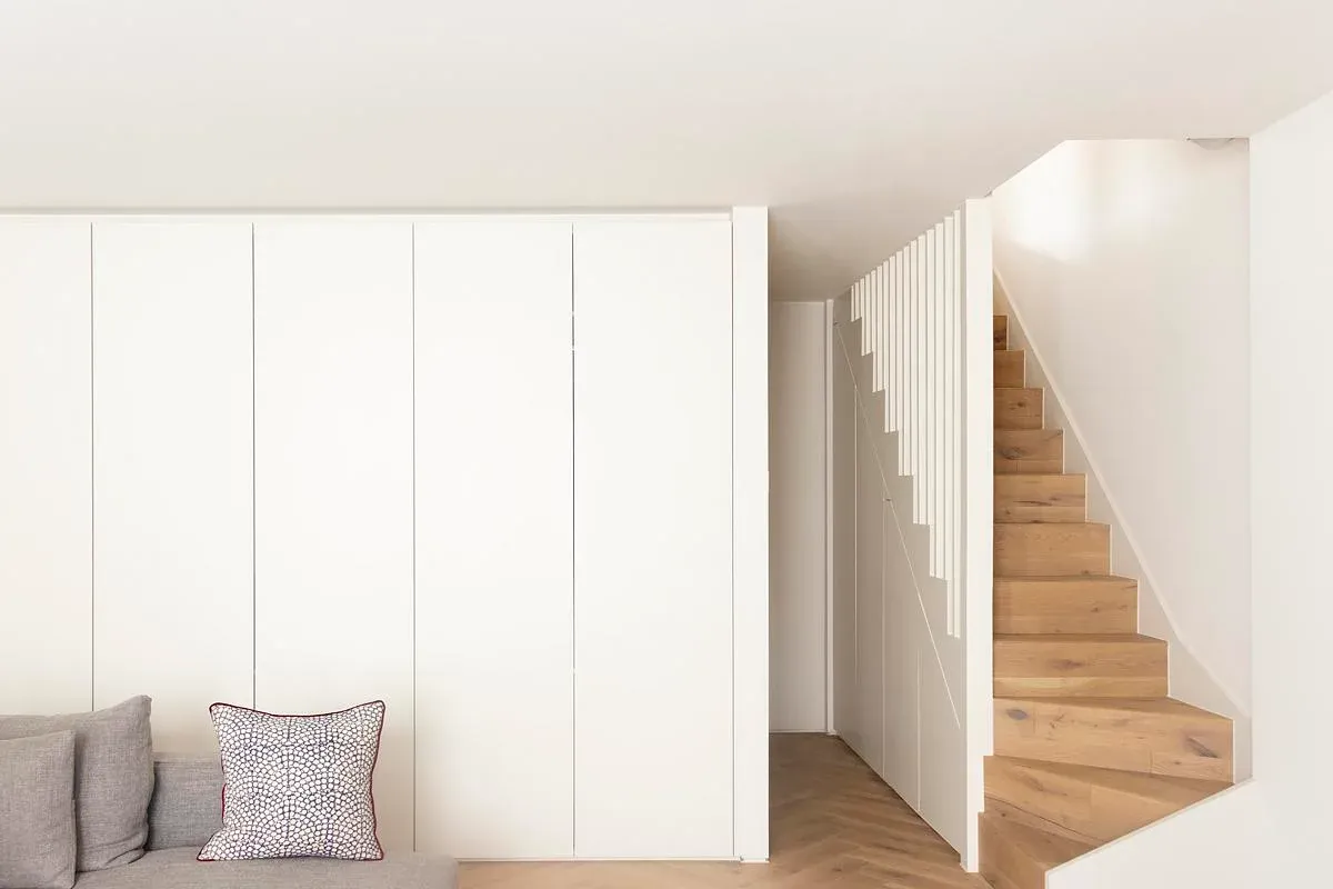 A white volume encloses storage beside the timber stair.