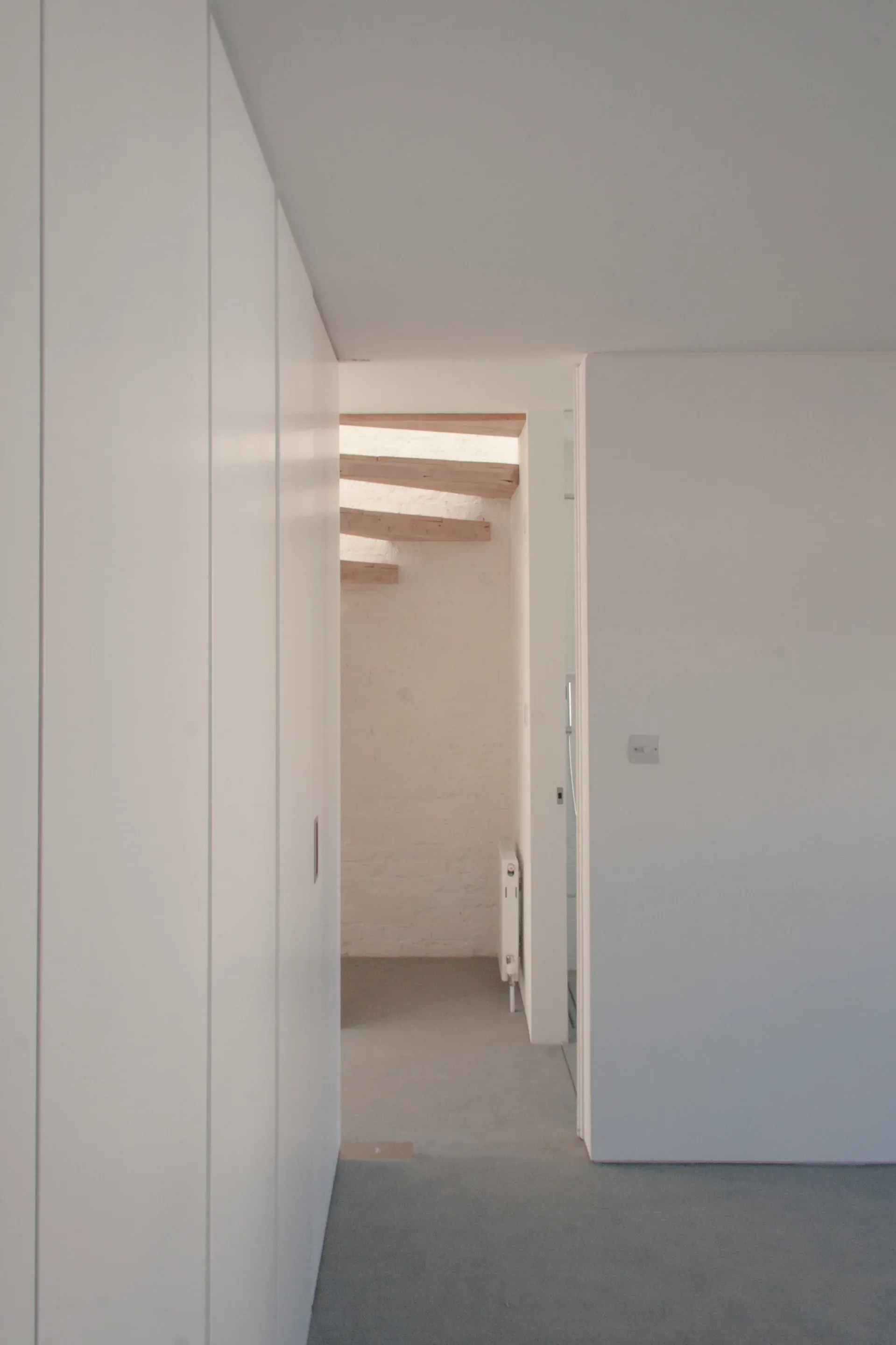 A doorway connects pale walls, grey carpet and exposed timber above.