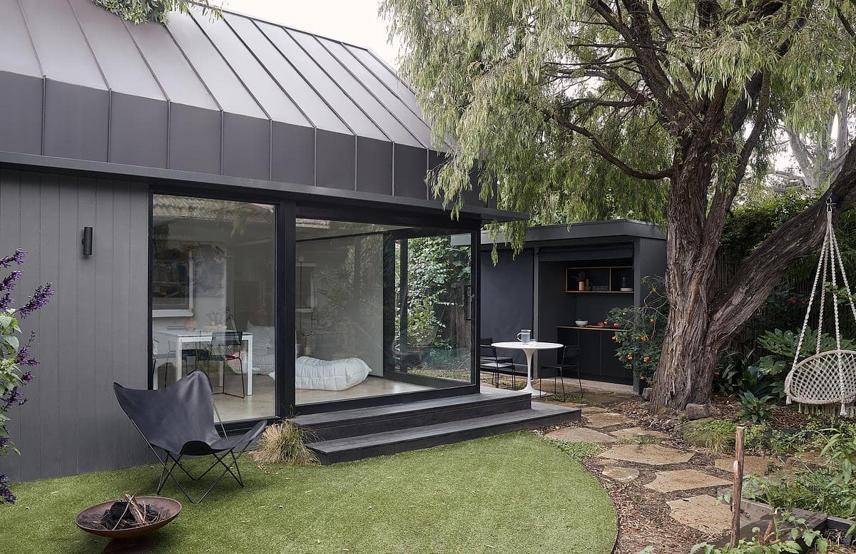 Large openings connect the dark-clad studio with its established garden.