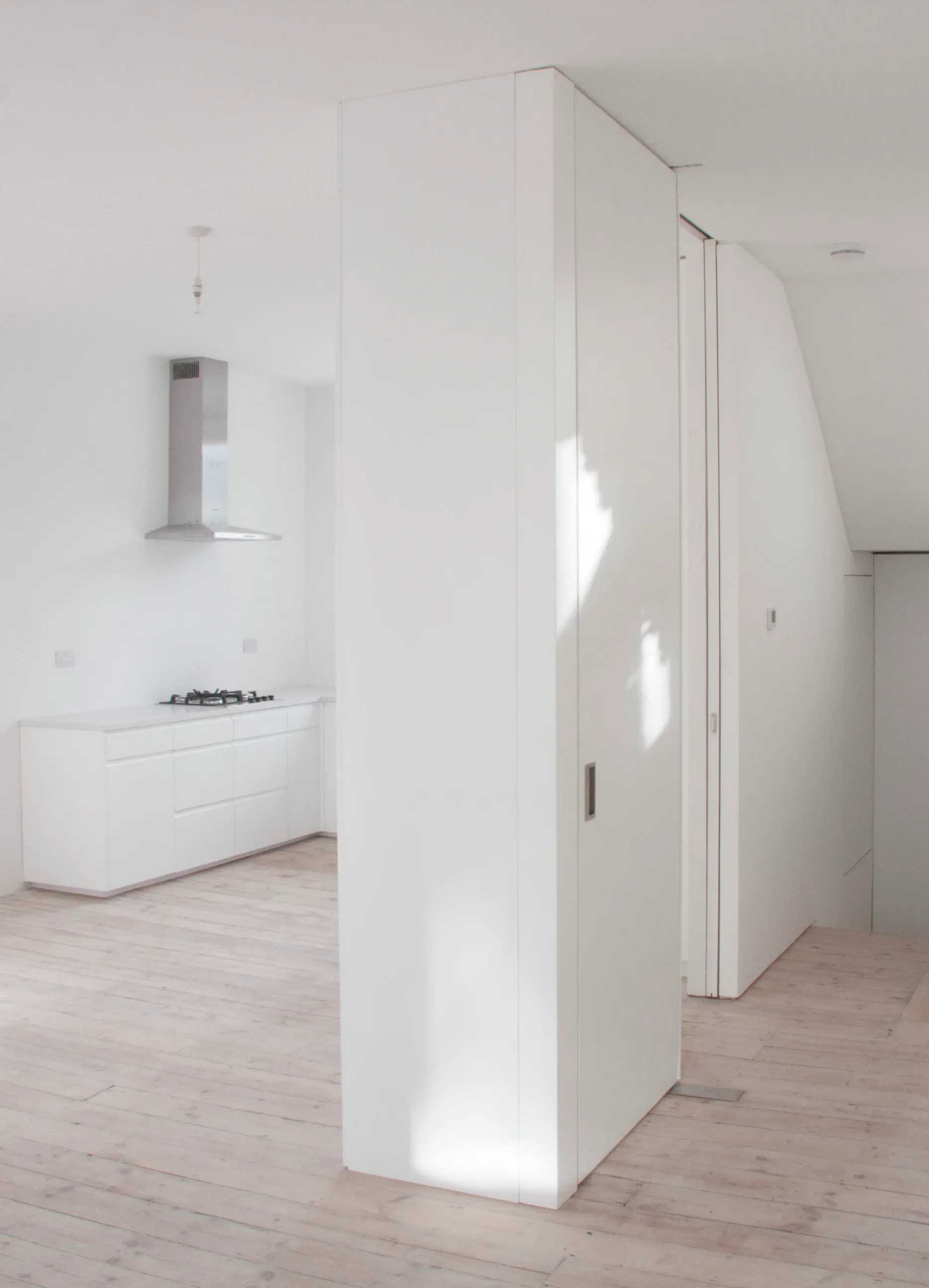White kitchen joinery forms a compact volume on the reclaimed timber floor.