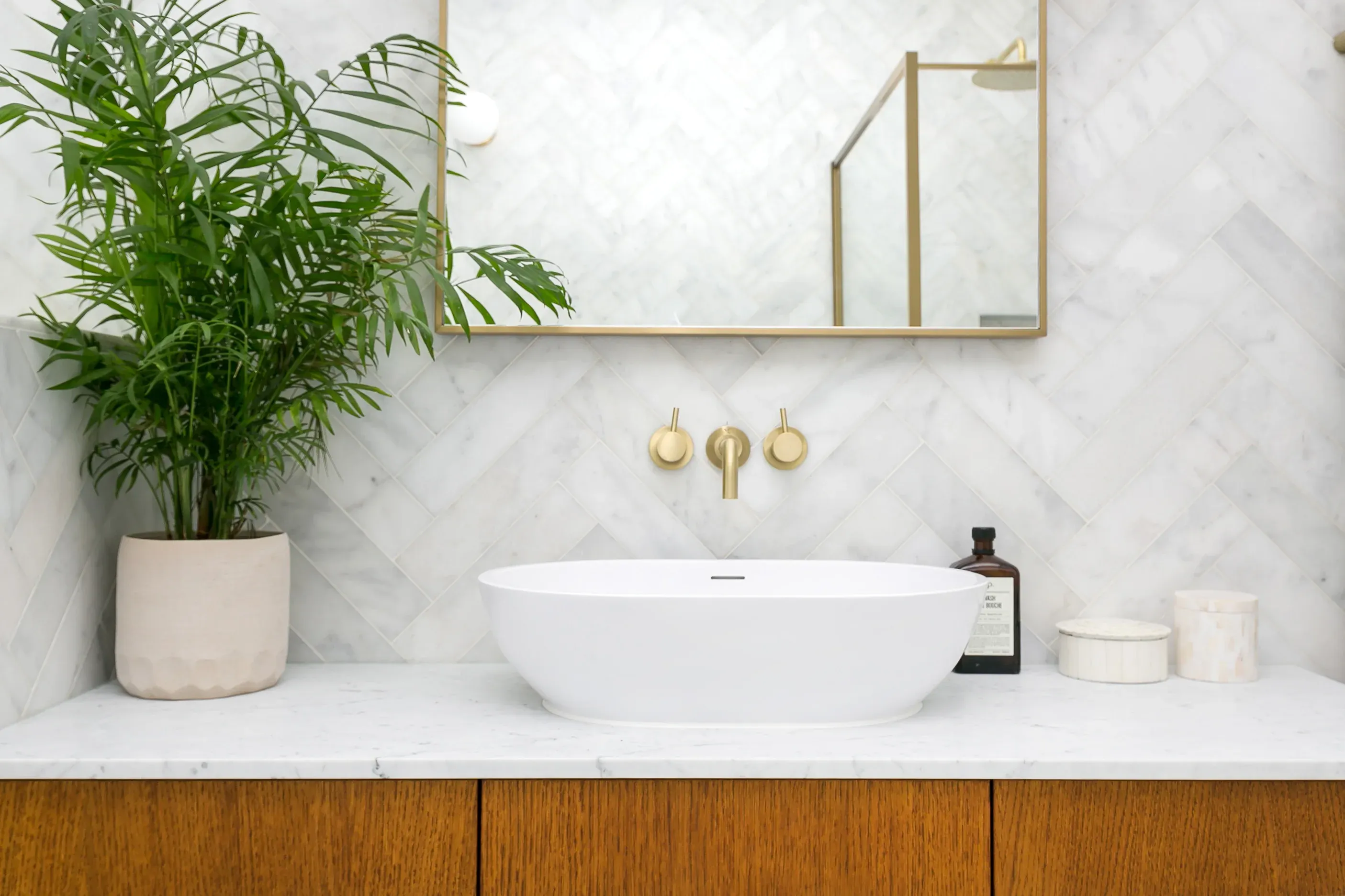 A white basin and brass fittings sit against a pale stone wall.