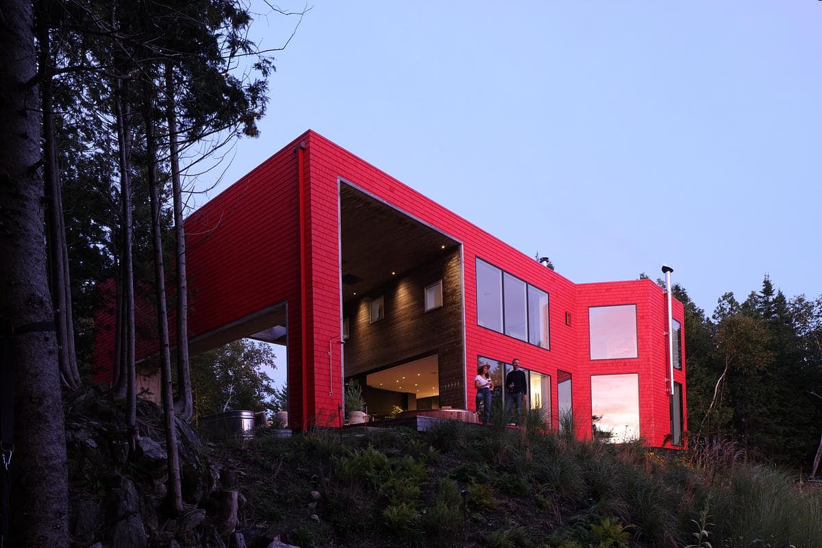 The covered outdoor room gives the red-clad house a deep, protected threshold.