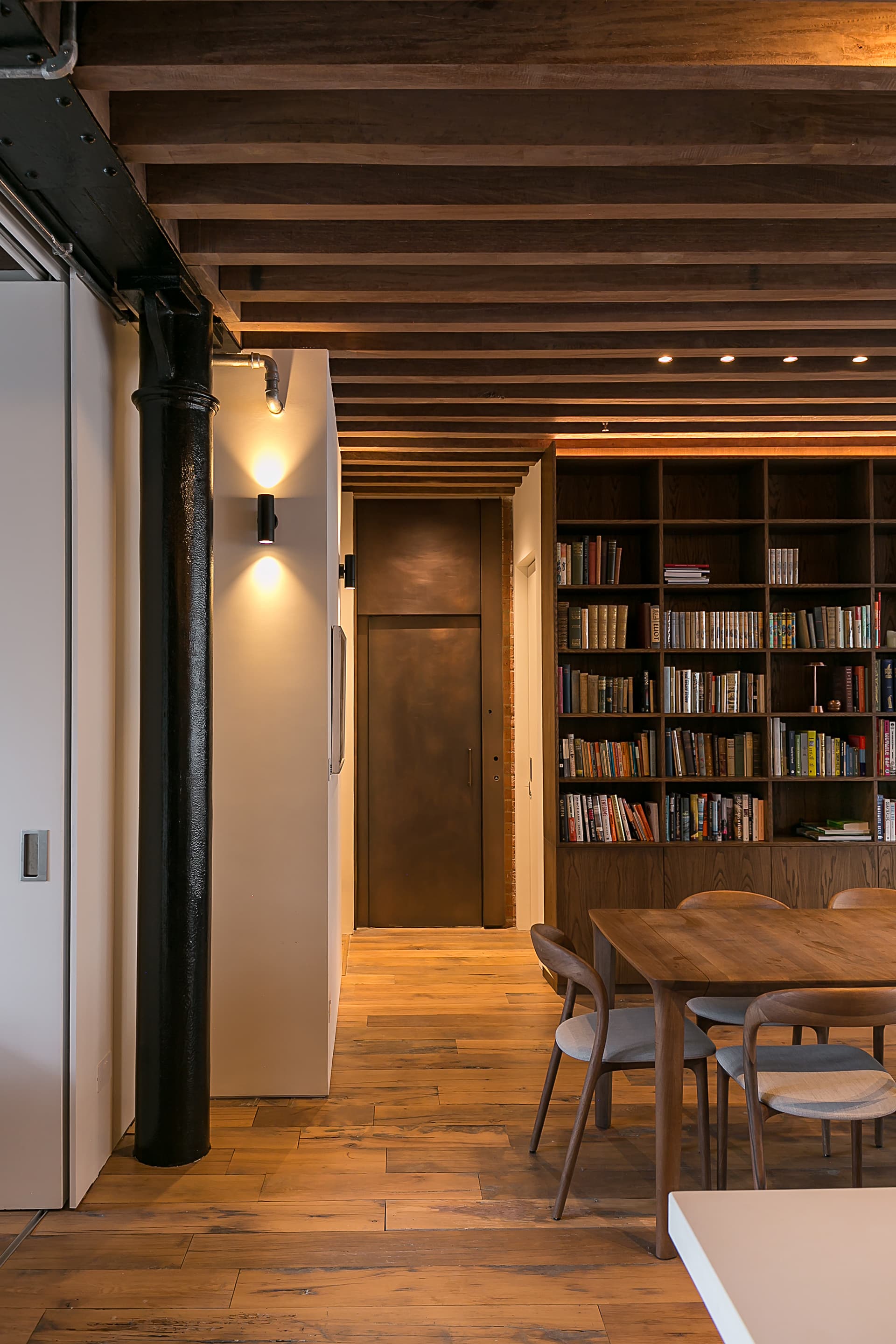 A steel column and fitted bookcase define the route beside the dining area.