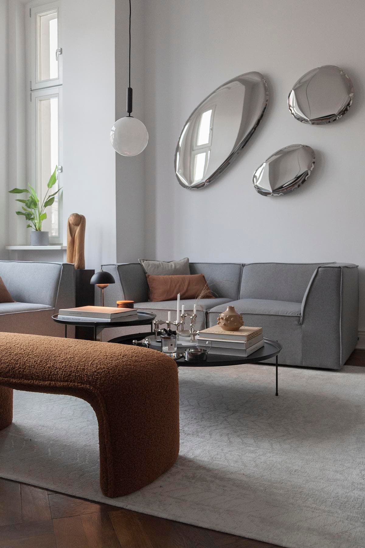 Sculptural mirrors and low furniture sit against the apartment’s tall windows.