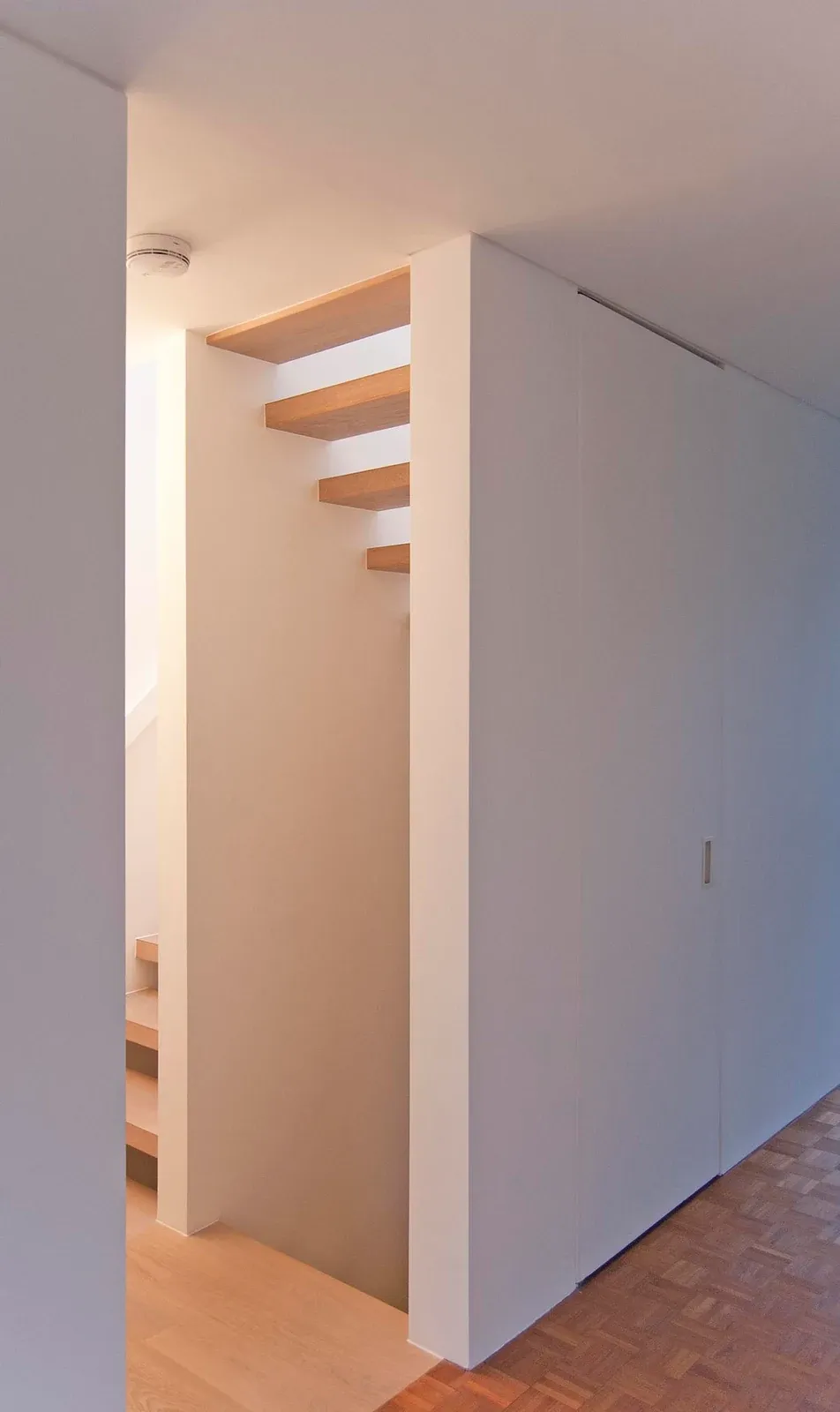 A white volume encloses part of the stair beside the parquet-floored landing at Modern Terrace.