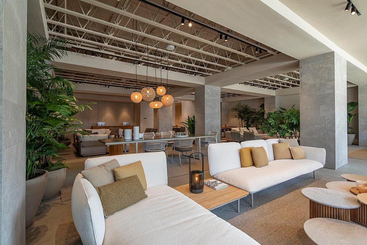 Outdoor furniture is arranged between planting and the exposed ceiling structure.