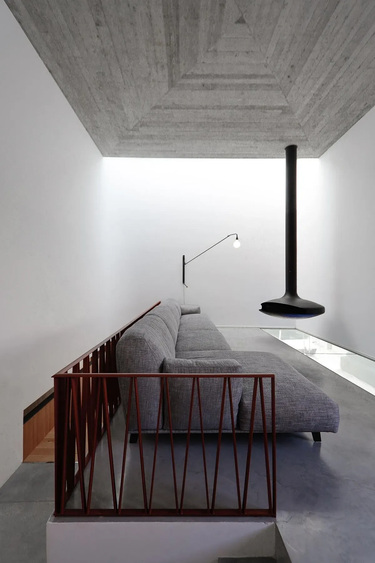 Board-marked concrete, white walls and a red steel balustrade frame the upstairs living room.