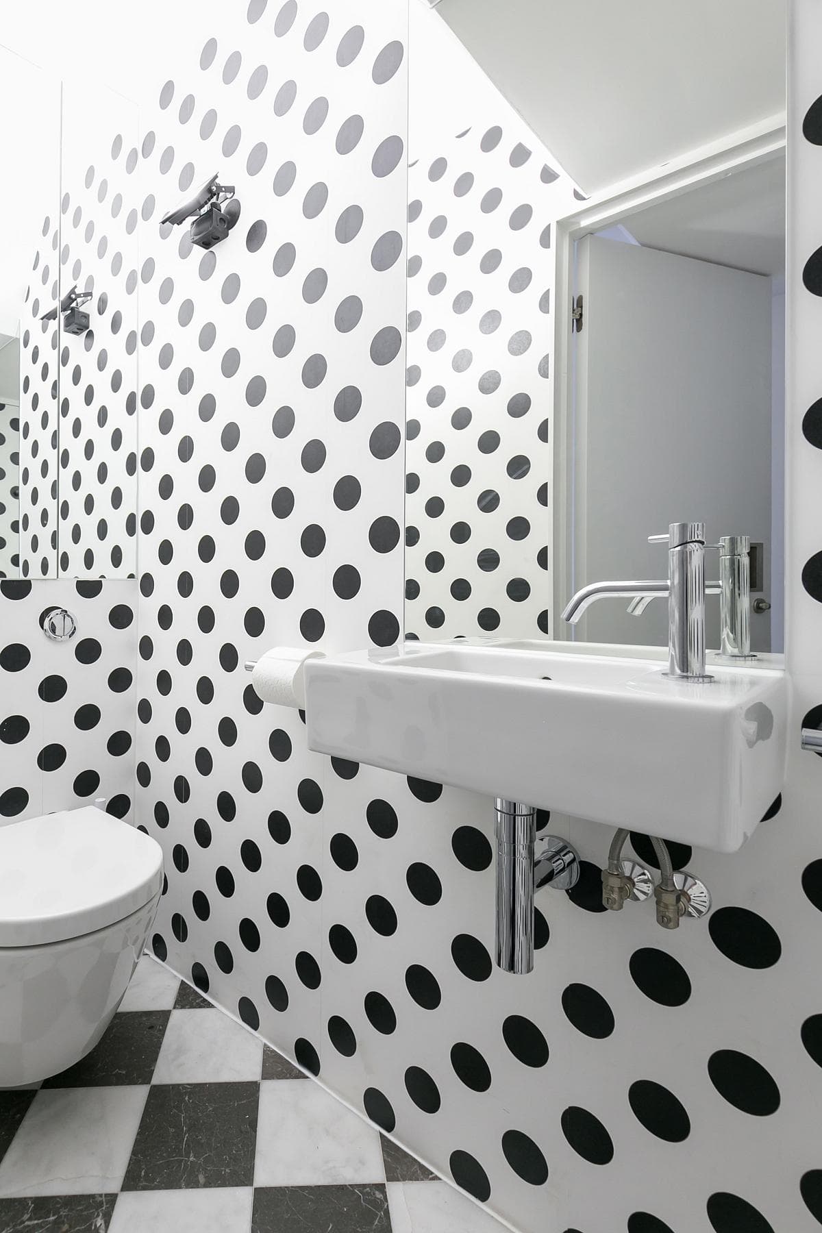 Black dots across white walls and a checkerboard floor define the small WC at House in Archway.