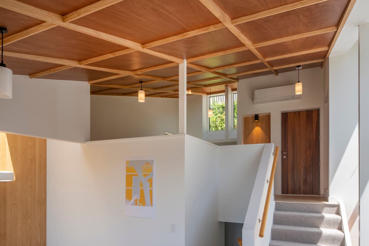 A continuous plywood ceiling connects the upper rooms and half-level stair.