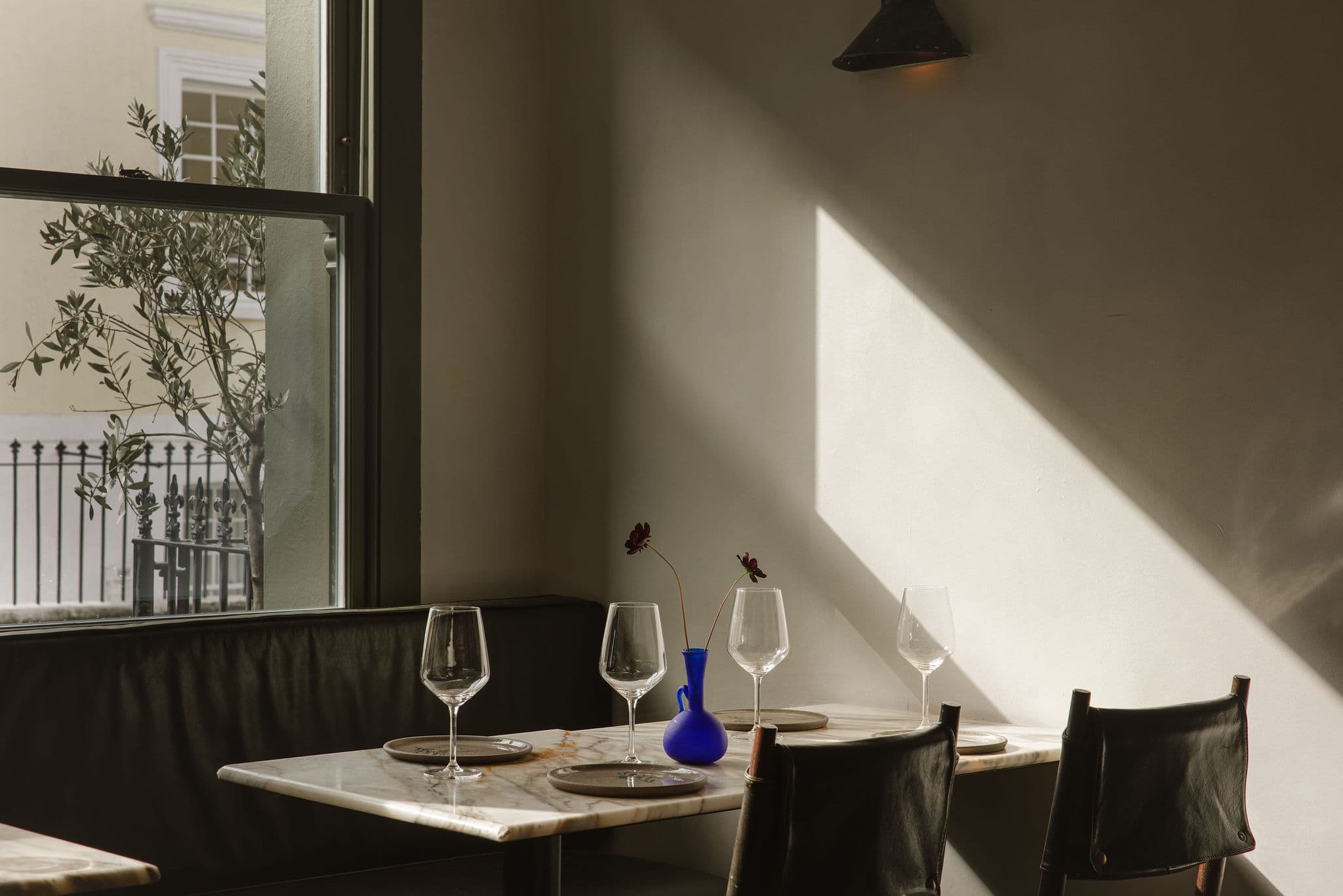 Daylight falls across a dining table and olive-green seating.
