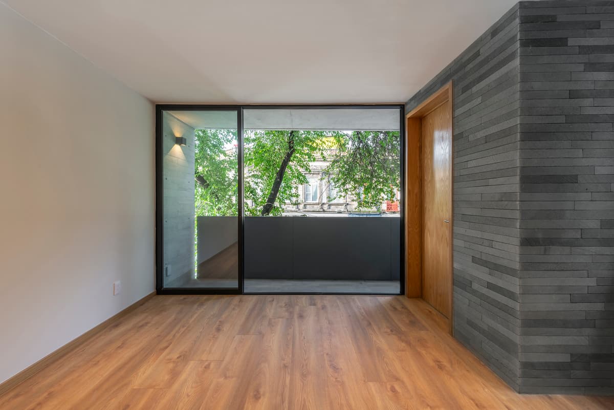 A living space opens towards the street-facing balcony and trees.