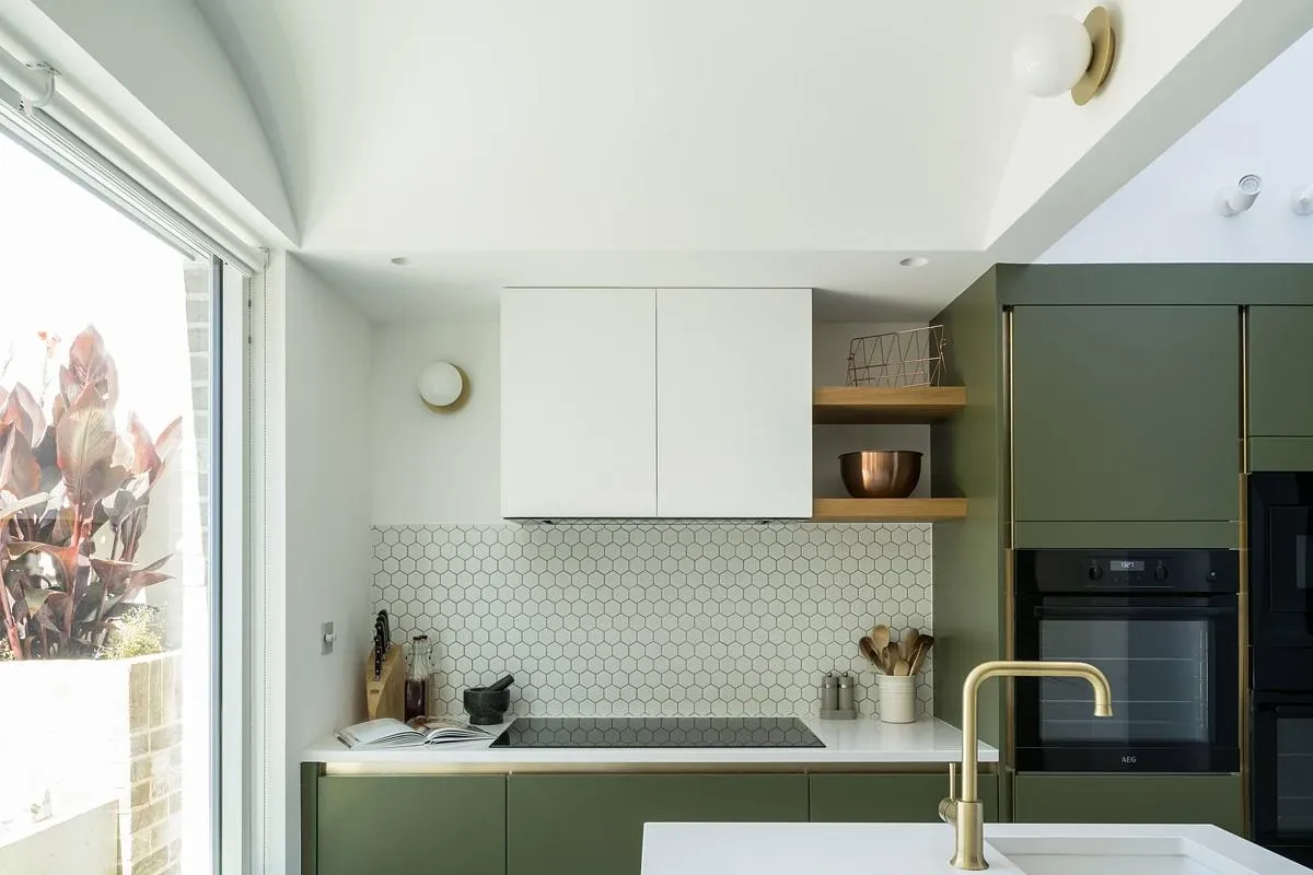 Green cabinetry, brass fittings and open shelving line the kitchen.
