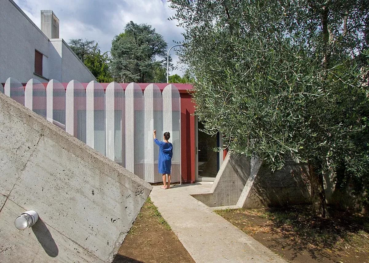 The cabin sits beside the garden, behind its folded perforated metal screen.