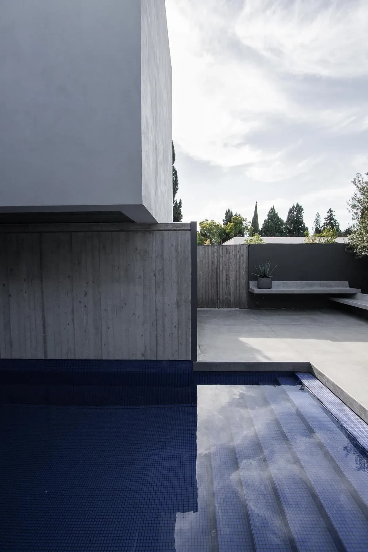 The pool sits beneath the white upper volume on the house's concrete and timber base.