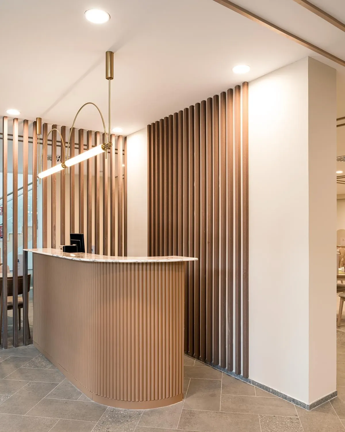 A curved timber reception desk stands between slatted screens.