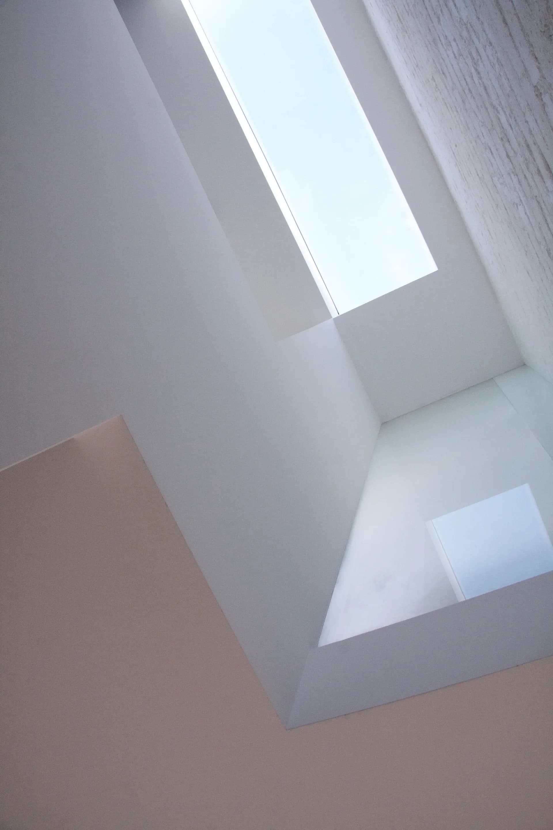 A deep rooflight brings daylight between the white planes of the upper floor.