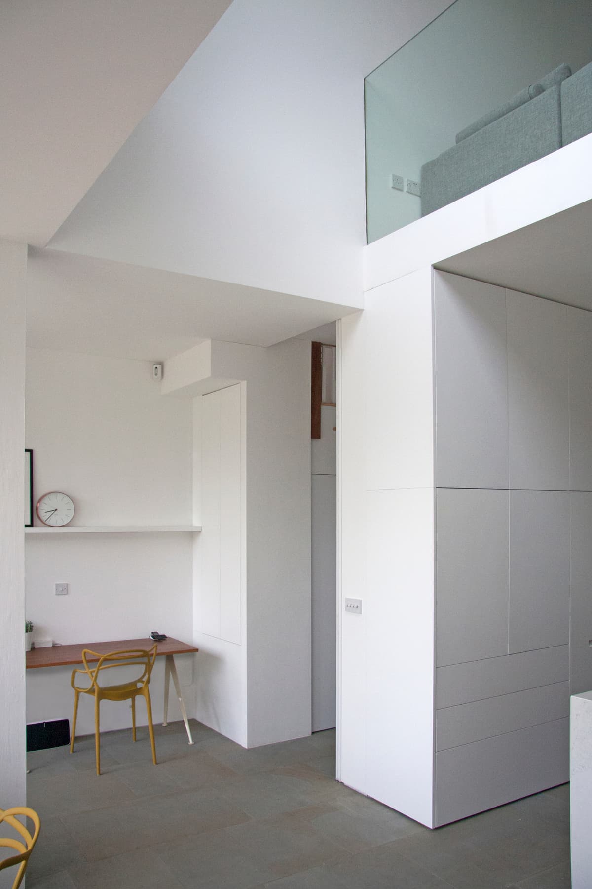 A glazed balustrade overlooks the lower living space beside a white storage volume at Vertical Intersect.