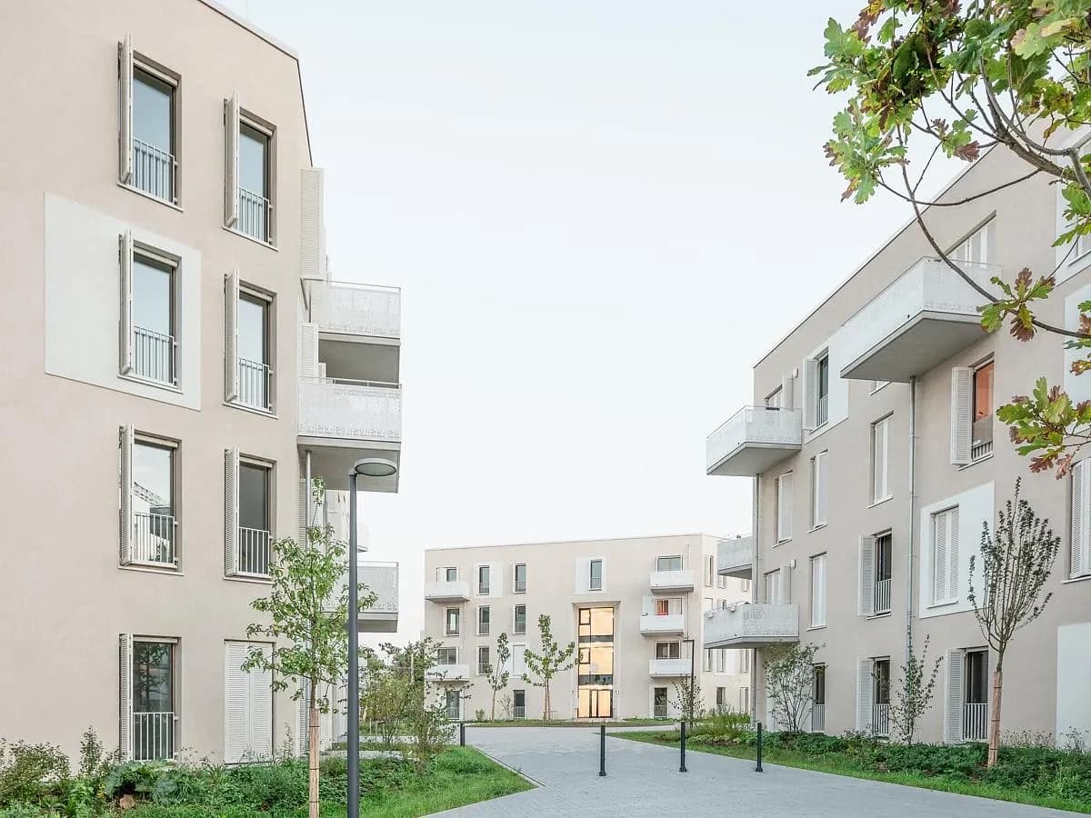 Plain rendered facades frame a landscaped route between the buildings.