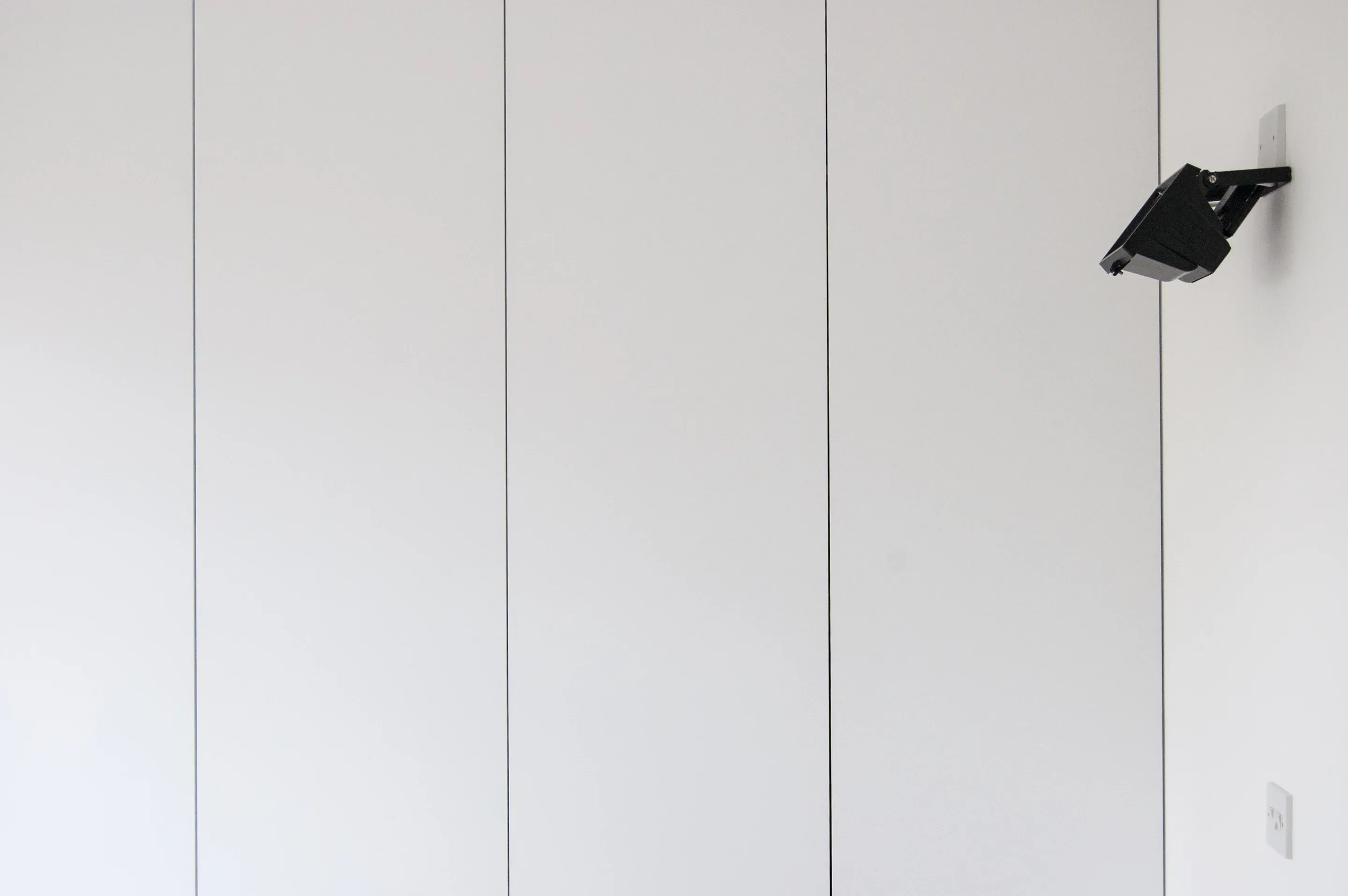 Concealed cabinetry forms a continuous white wall beneath a small wall light.