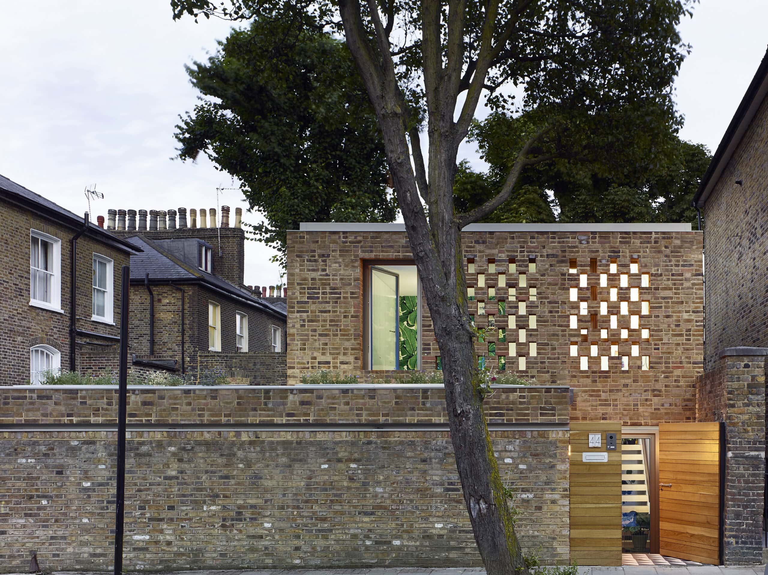 Front of the brick house behind a tree.