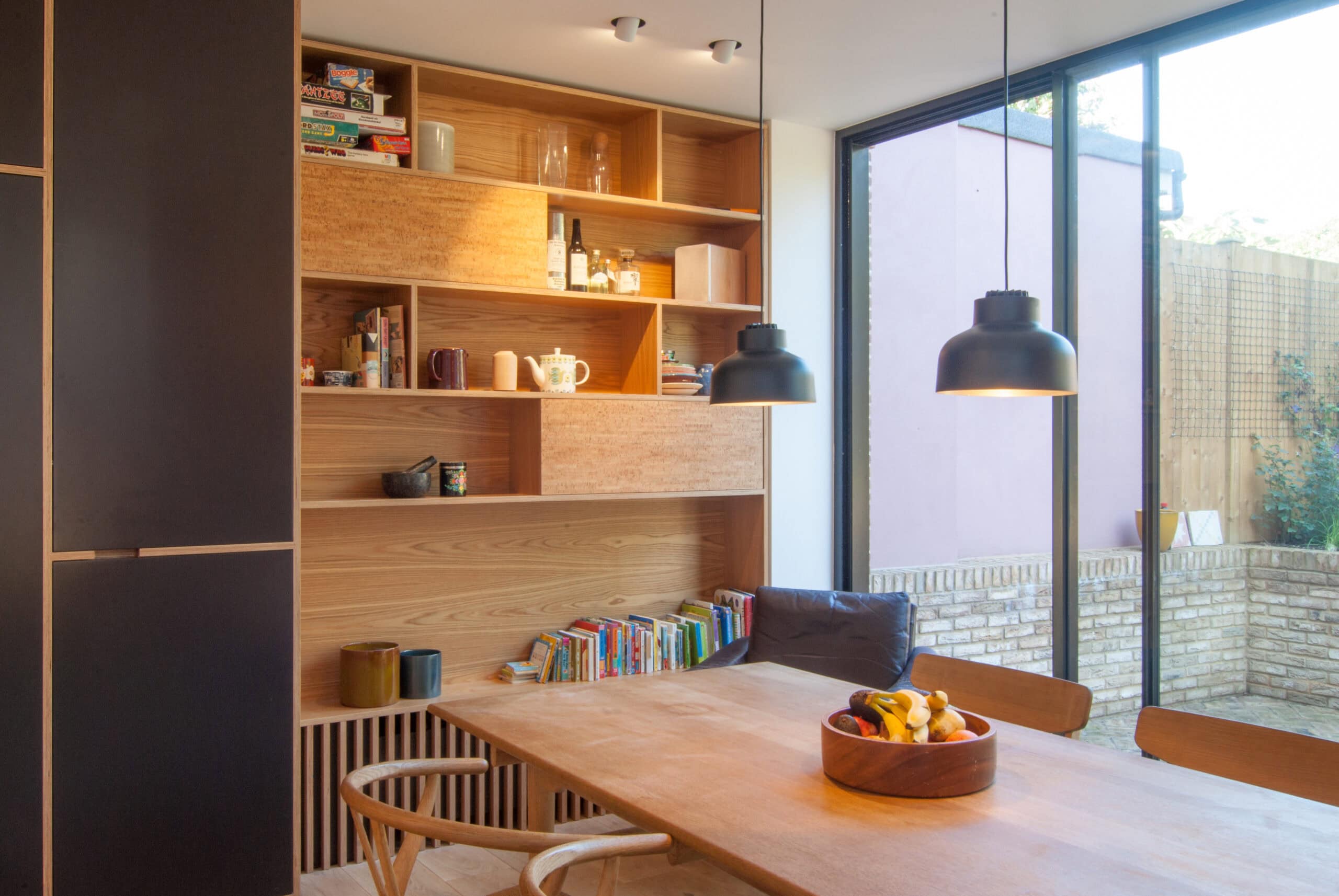 Dining table beside shelving and garden glazing.