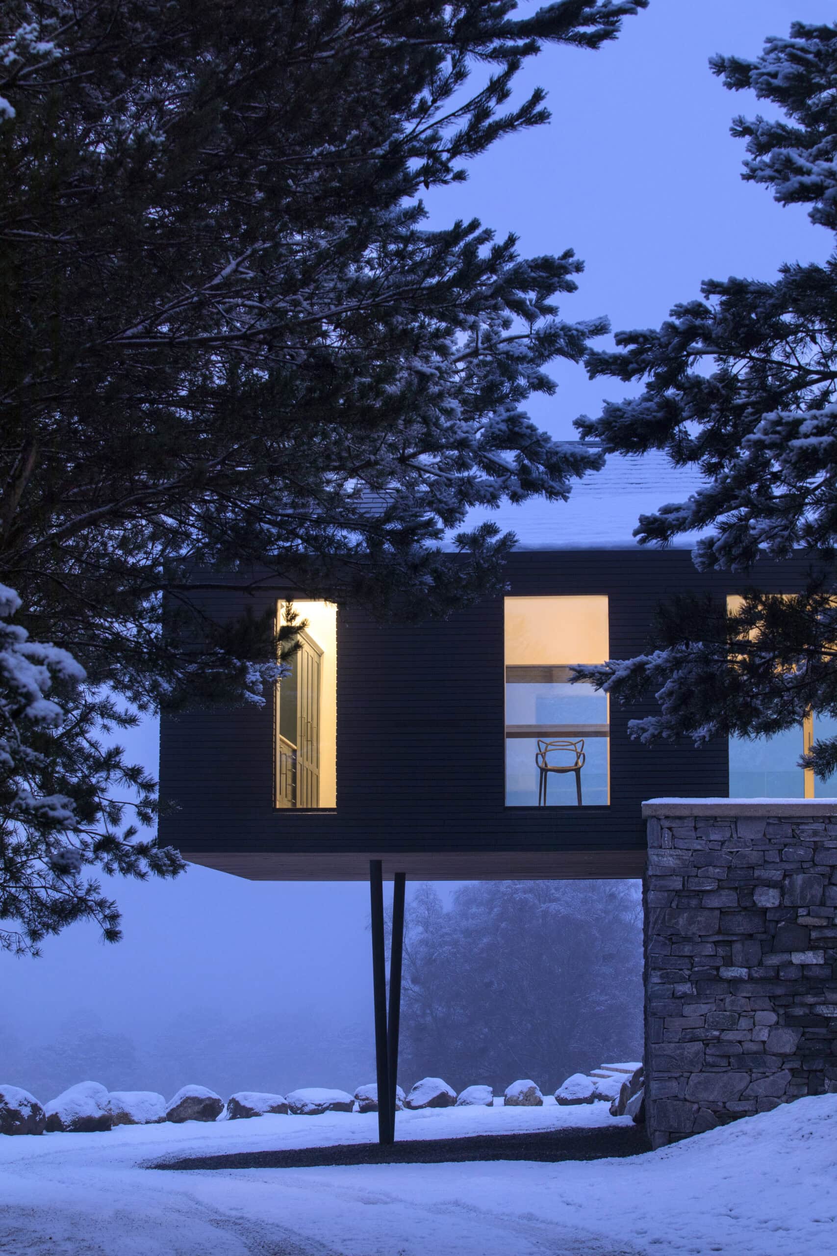 Illuminated timber-clad upper storey above a stone base in the snow at dusk.
