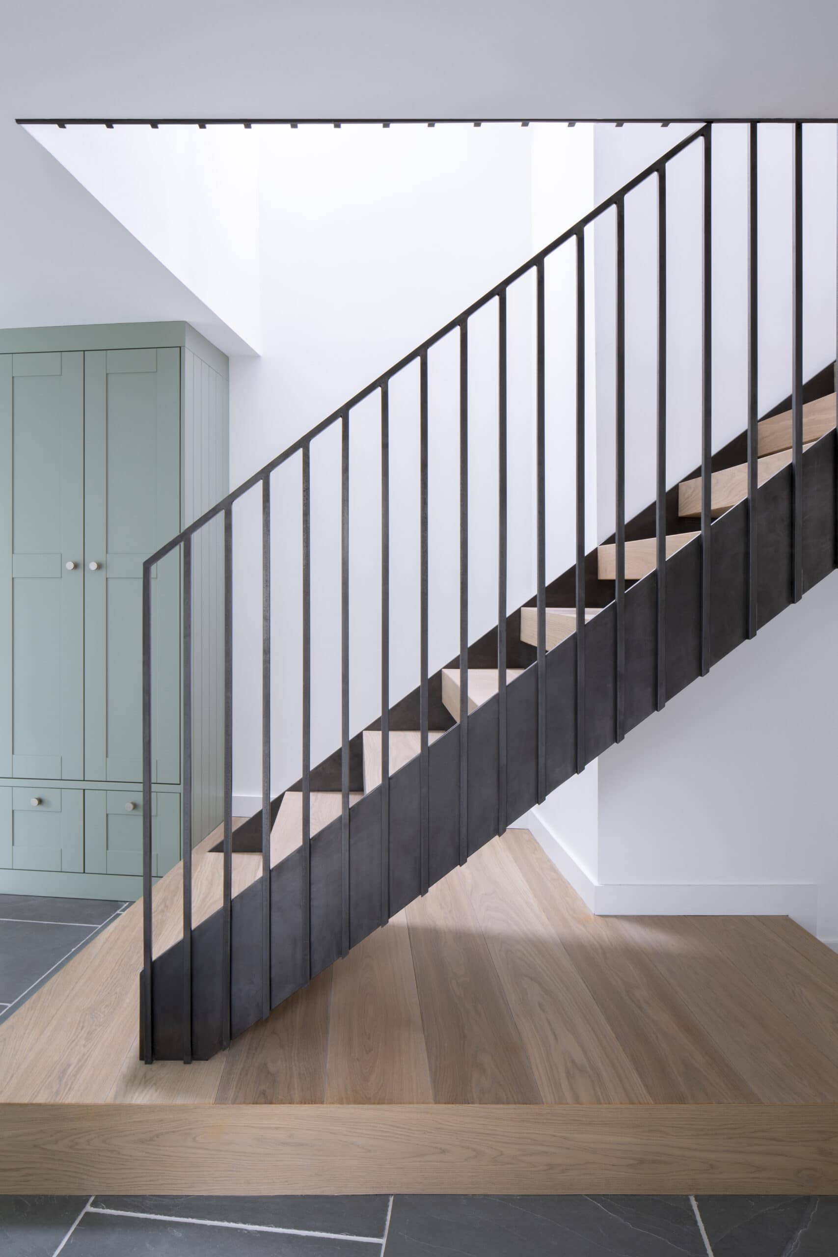 Timber staircase with slender black balusters beside a pale green door.