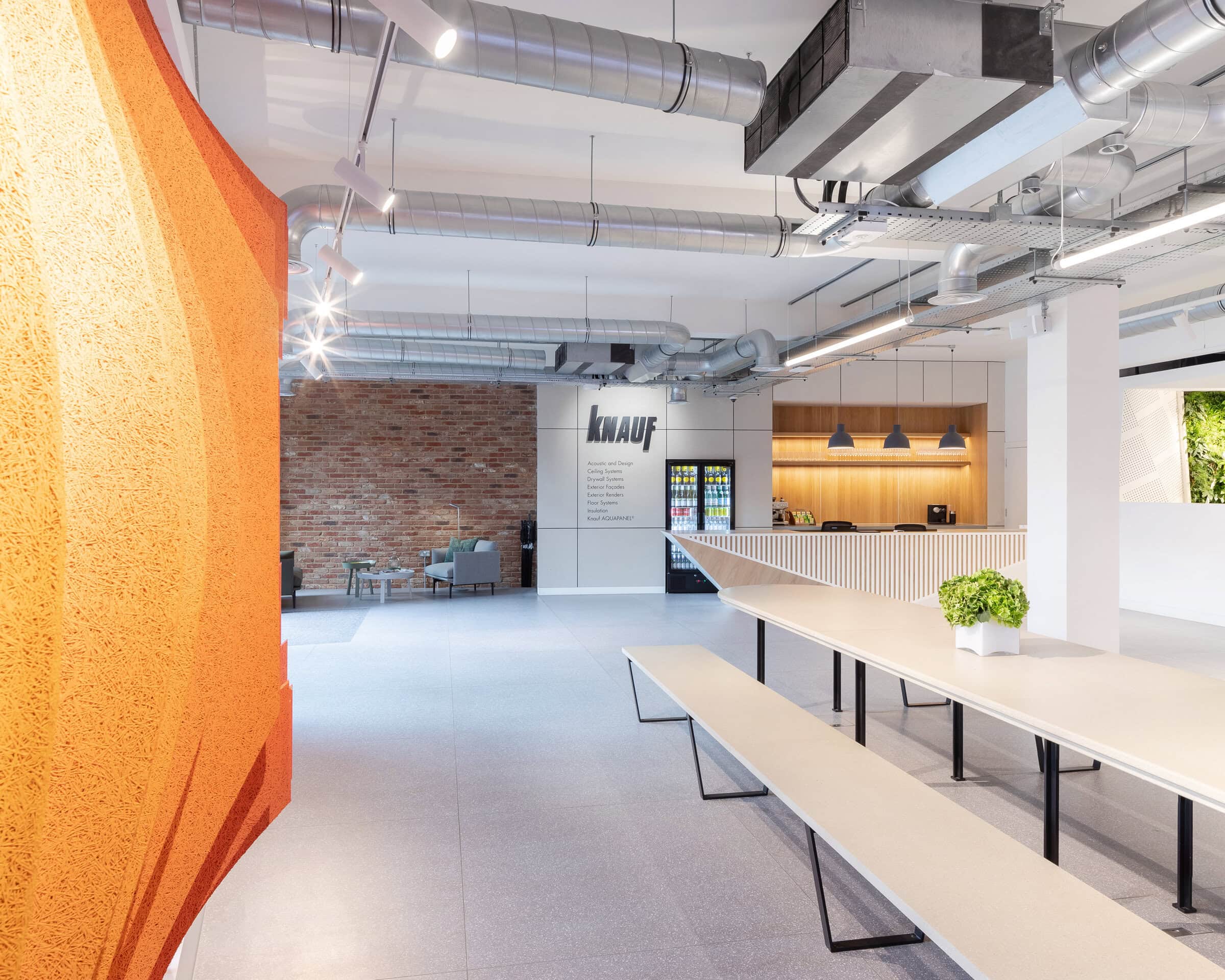 Wide workplace interior with timber tables and an orange wall.