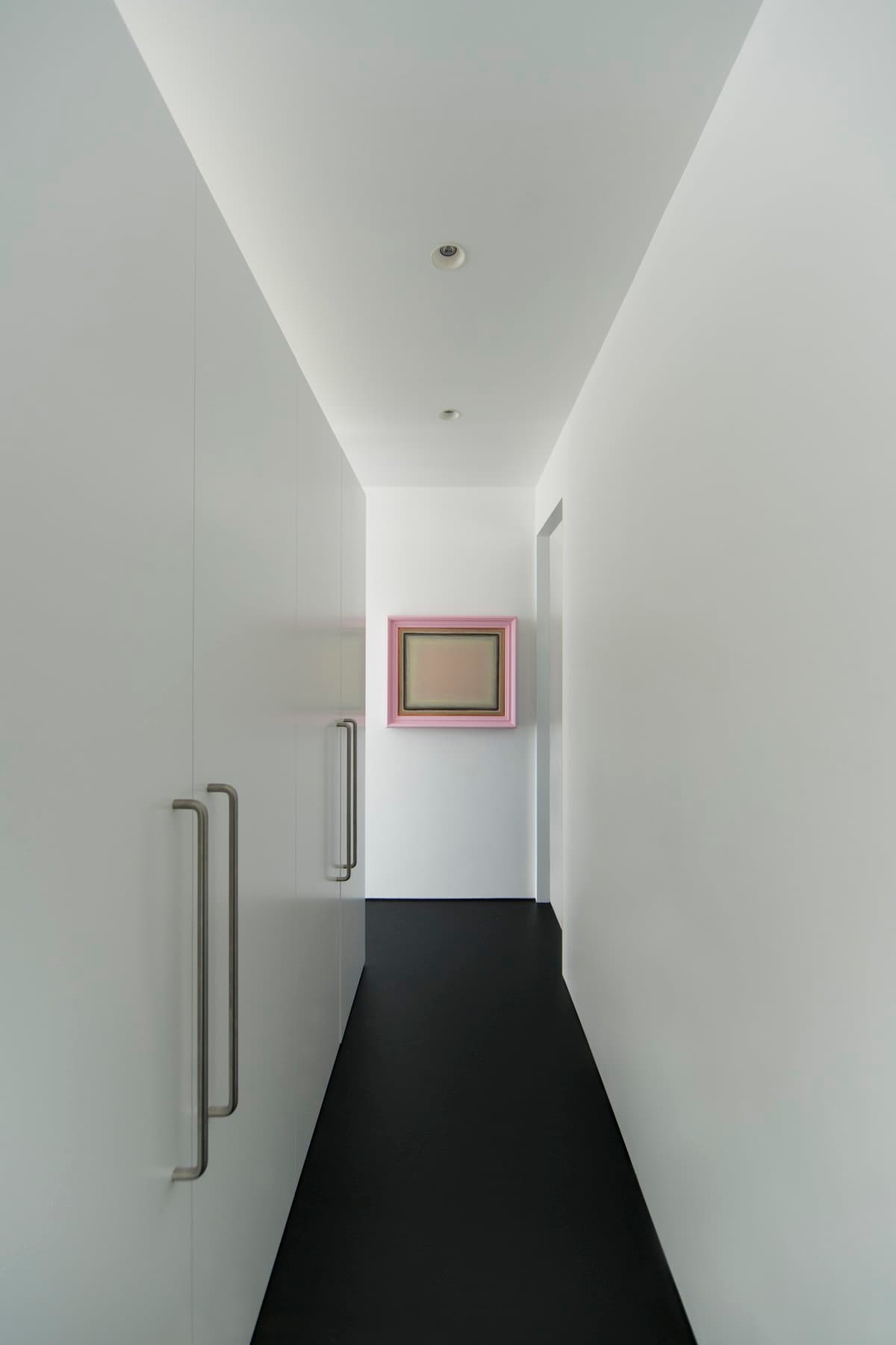 Modern minimalist hallway with white walls, dark floor, and framed artwork at the end.