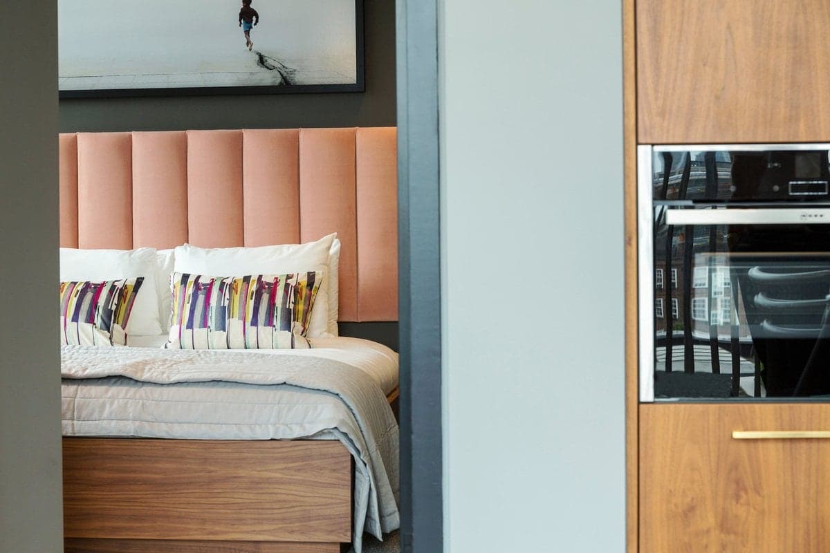 Stylish bedroom with peach headboard, modern art, and adjacent wooden cabinetry kitchen area.