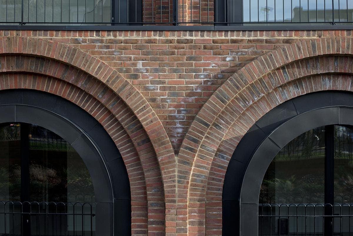 Red brick arches with black metal frames and reflective glass windows below.
