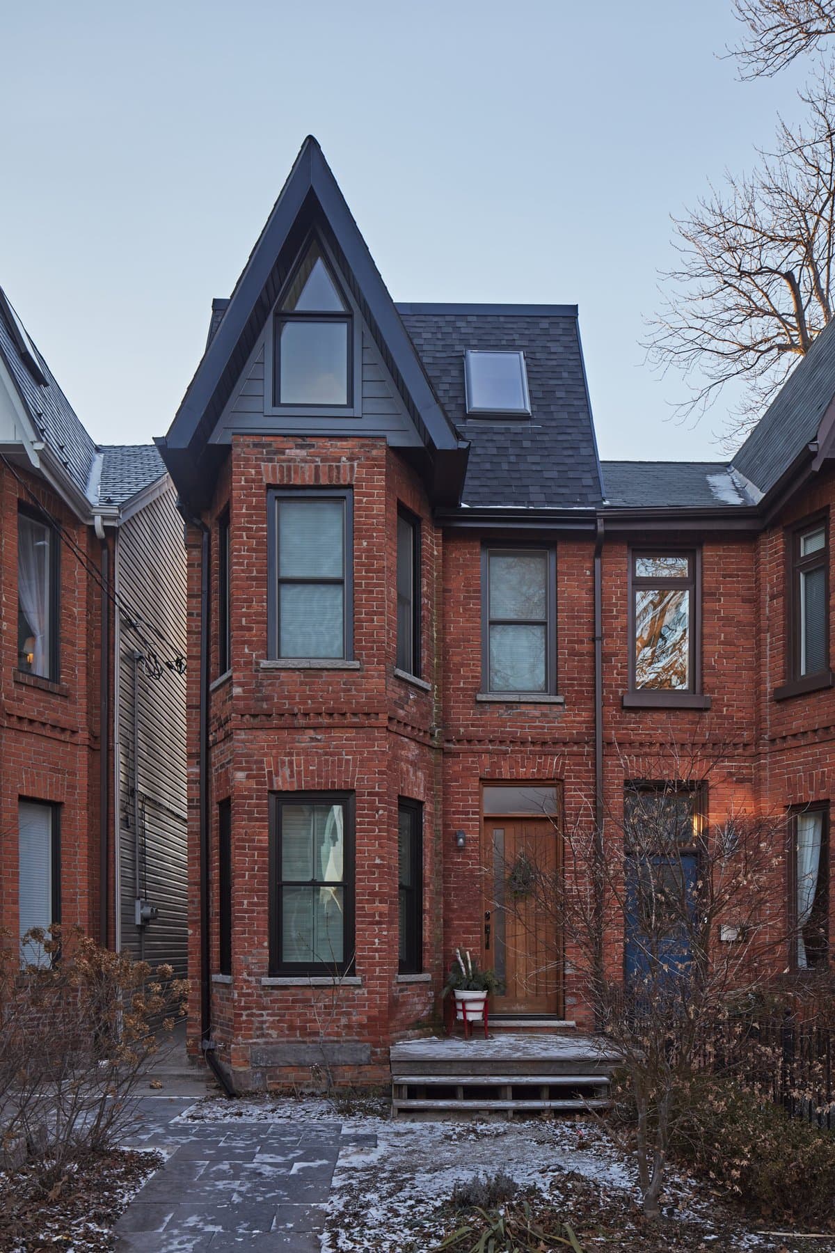 Red brick townhouse with modern gable, winter setting, narrow windows, frosty garden.