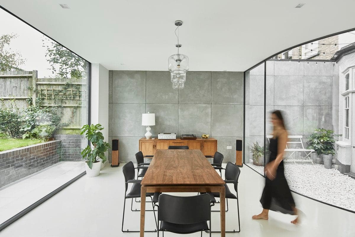 Modern minimalist dining room with natural light, wooden table, black chairs, and garden view.