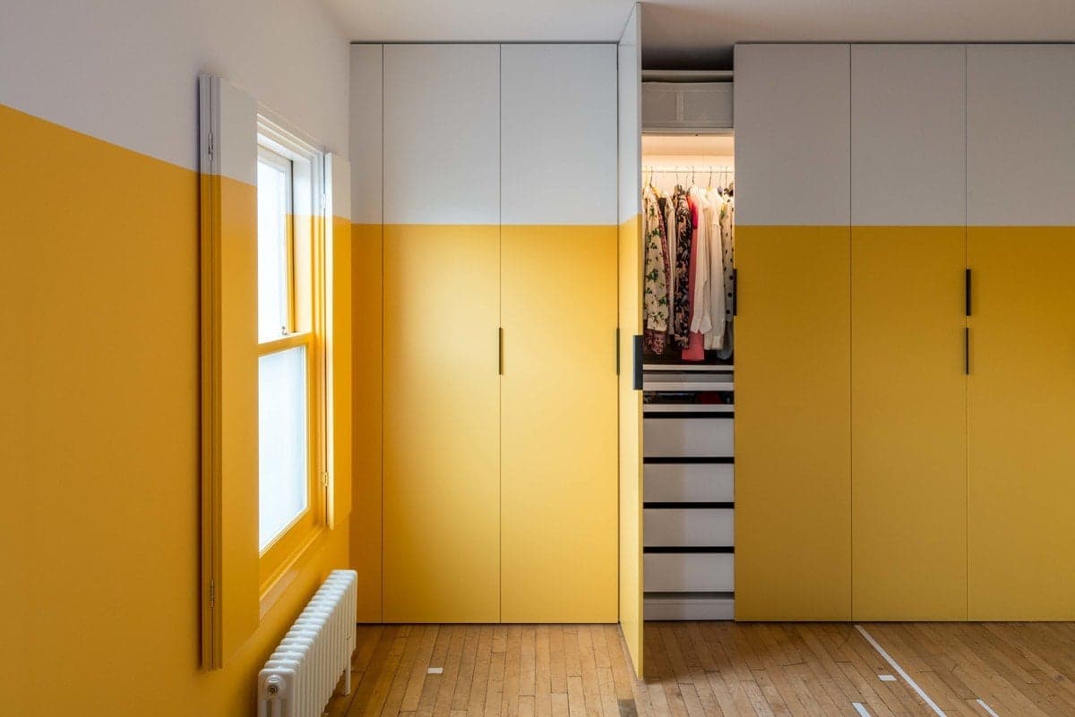 Modern minimalist room with yellow and white decor, natural light, and organised wardrobe.