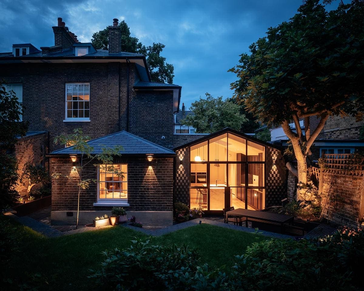 Cozy brick home at dusk with modern glass extension and inviting garden atmosphere.