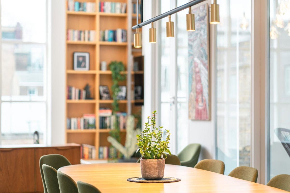 Dining table with chairs and pendant lights beside large windows.