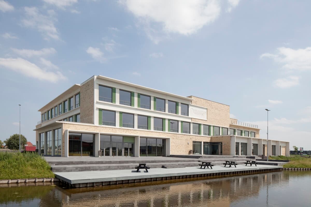 Modern multi-story building with picnic area and water feature, VMBO Melanchton Berkroden.